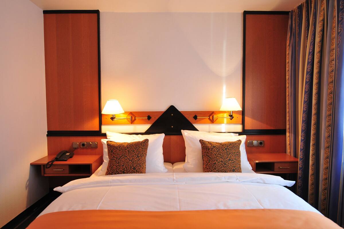 A hotel room with a large bed, two bedside tables, a nightstand, and a decorative wall panel.