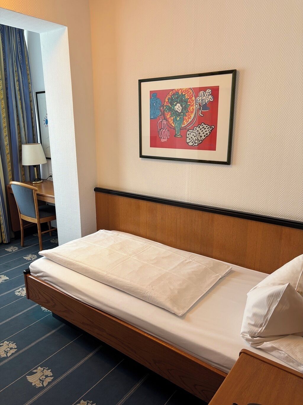 Habitación de hotel con cama, escritorio, silla y una obra de arte colgada en la pared.