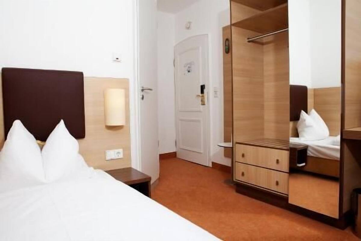 A hotel room with a bed, a wardrobe, a mirror, and a nightstand.