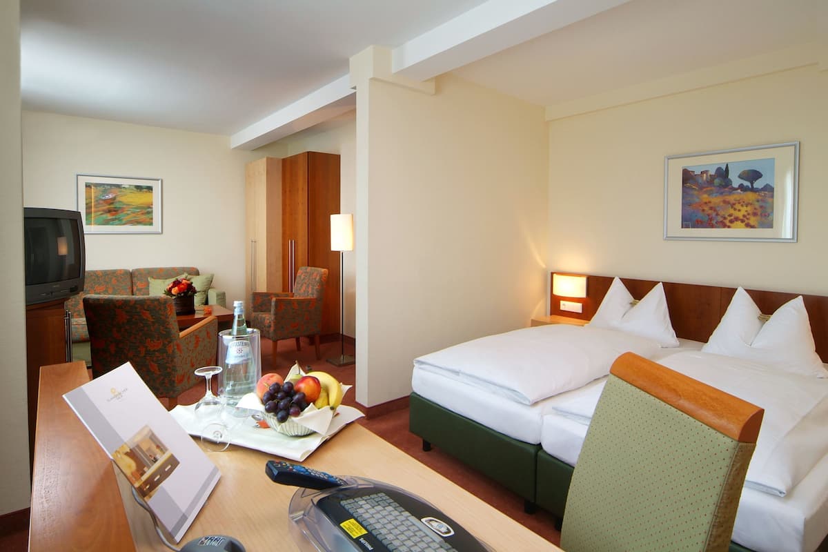 A hotel room with a bed, a desk with a remote control, a chair, a television, and artwork on the walls.