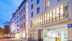 Un hotel con fachada moderna, grandes ventanales y entrada de estacionamiento visible.