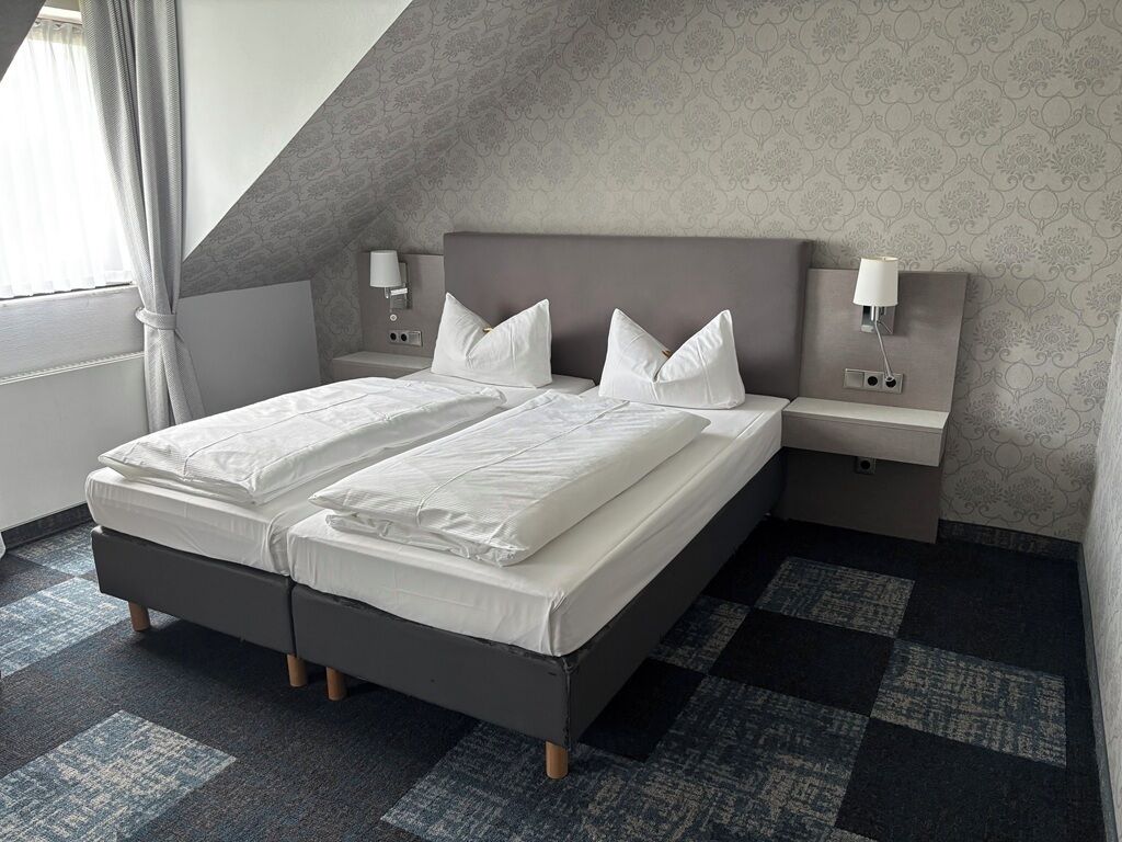 A double bed with two nightstands, each with a lamp, in a room with patterned wallpaper and a checkered carpet.