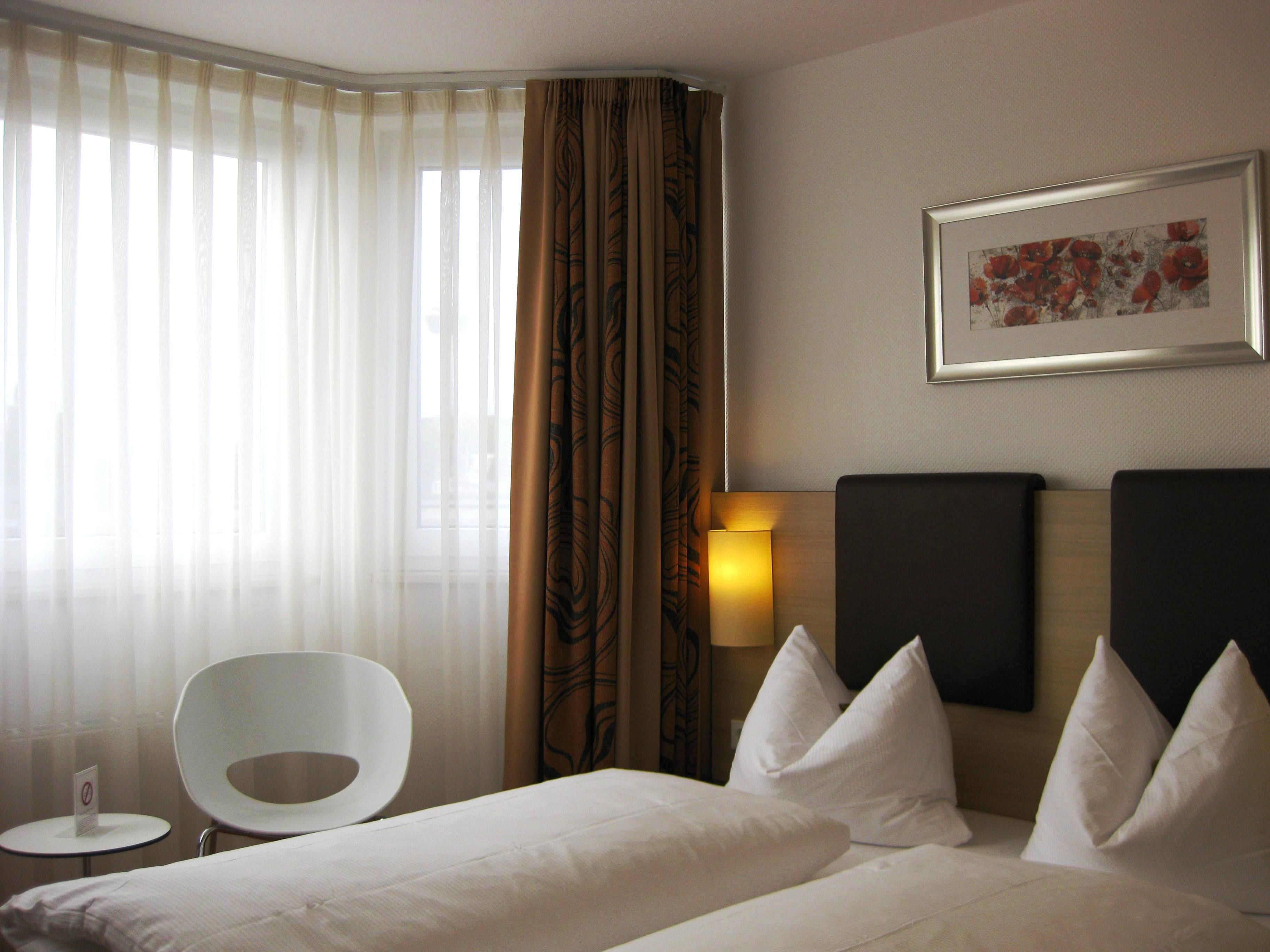 A hotel room with a bed, a chair, a lamp, and a painting on the wall.