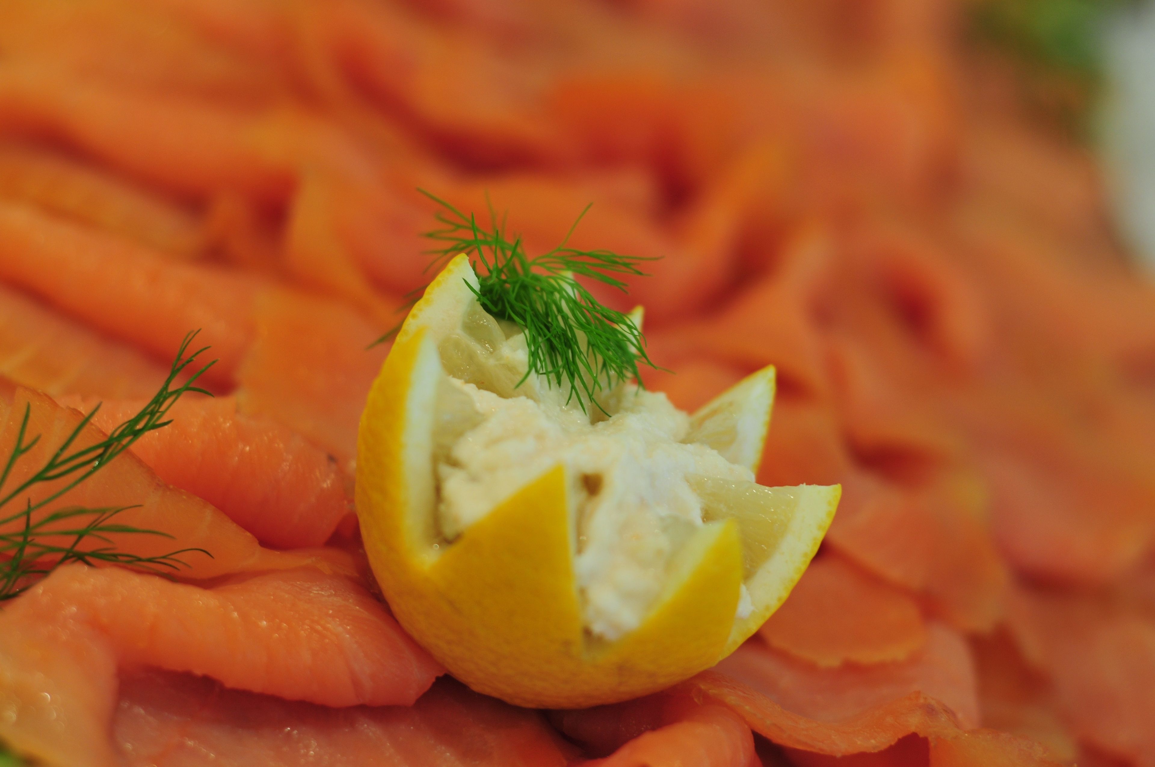 A close-up of a lemon half filled with a creamy substance, garnished with dill, surrounded by slices of salmon.