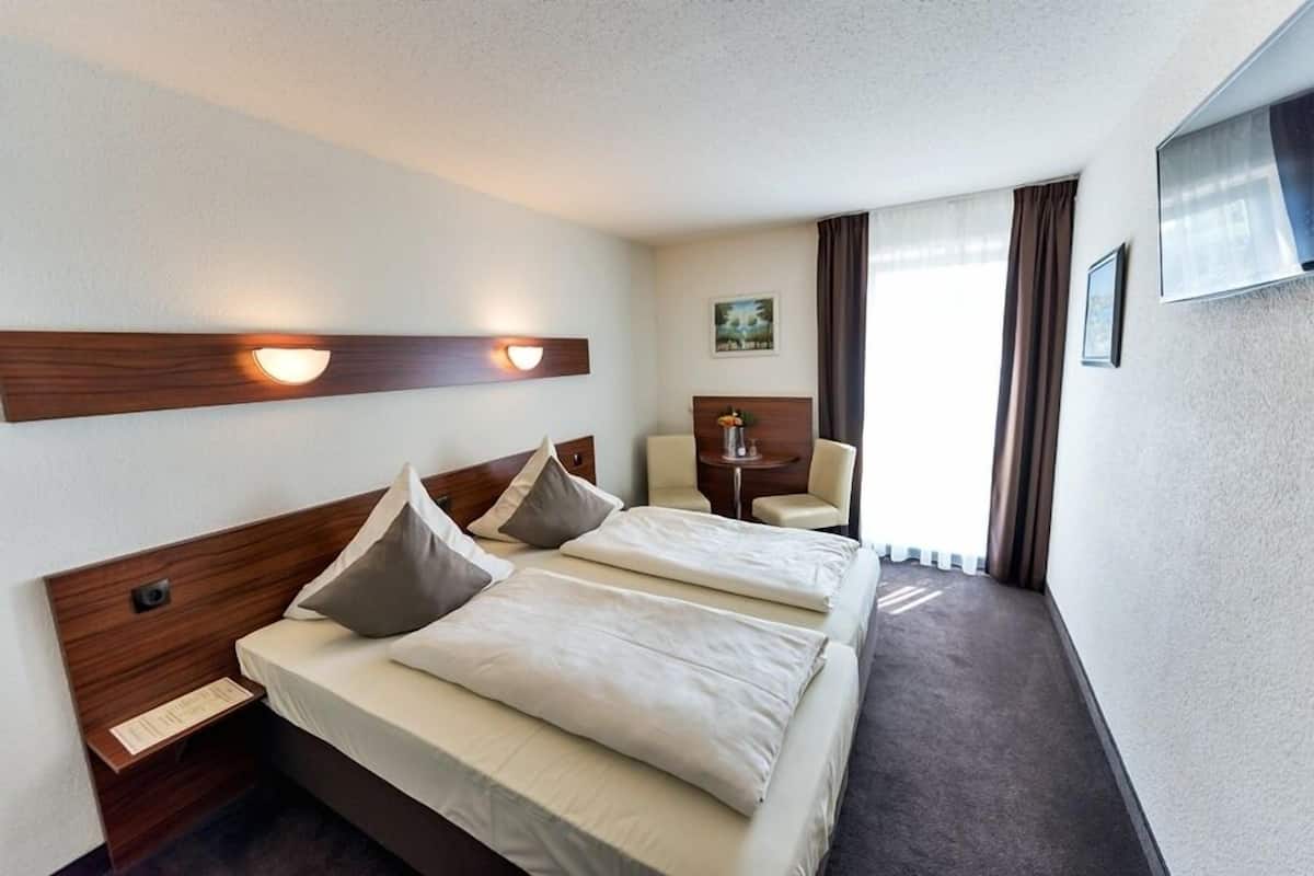 A hotel room with two beds, a desk, a chair, and a TV on the wall.