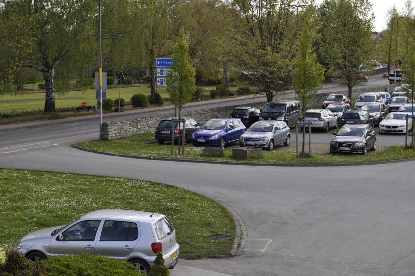 A parking lot with multiple cars and a road curving around it.