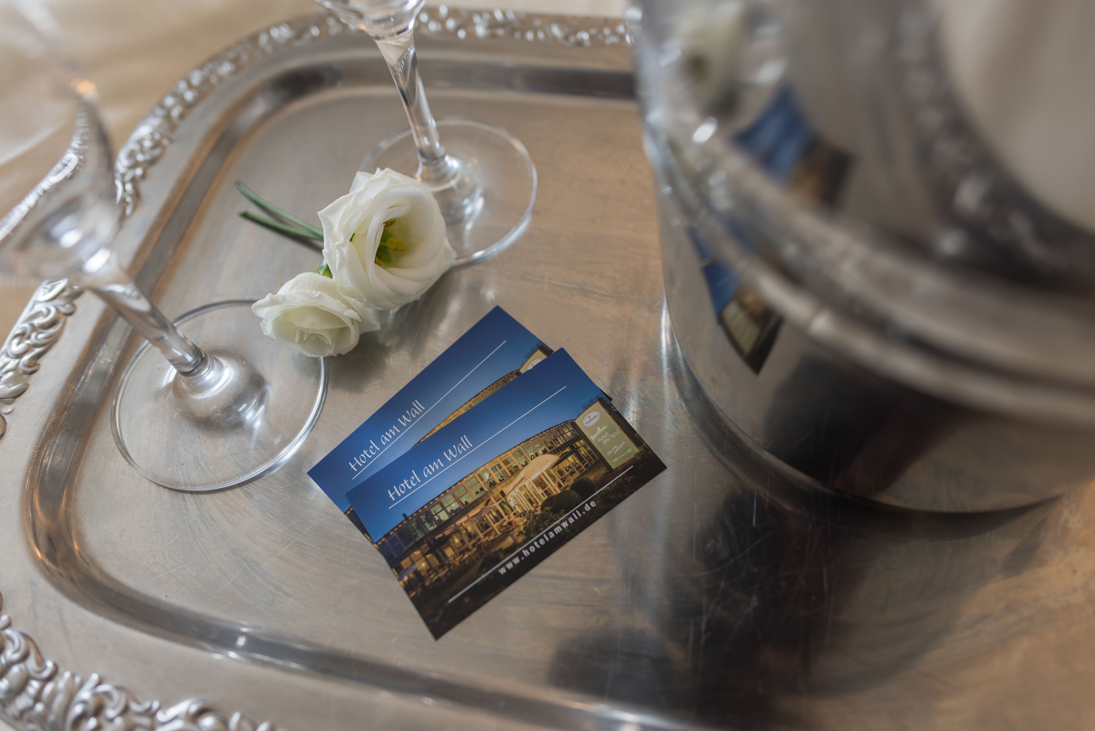 A silver tray with a glass and a white rose, a business card, and a silver container.