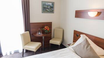 A hotel room with a bed, two chairs, a small table with a vase of flowers, a painting on the wall, and a nightstand with a lamp.