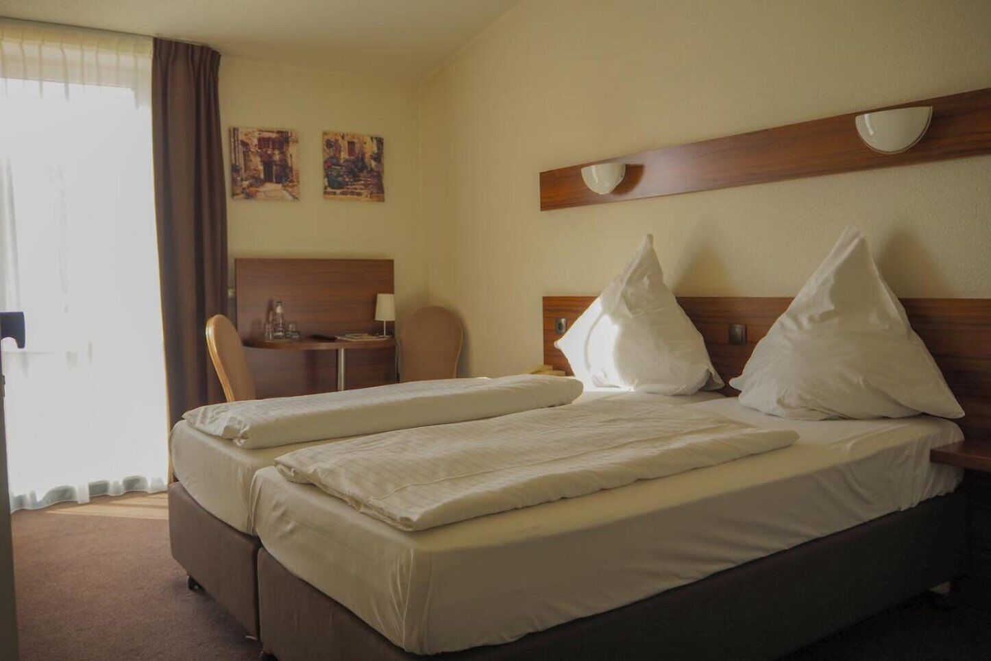 Une chambre d’hôtel avec un lit double, un bureau avec une chaise et deux lampes fixées au mur.