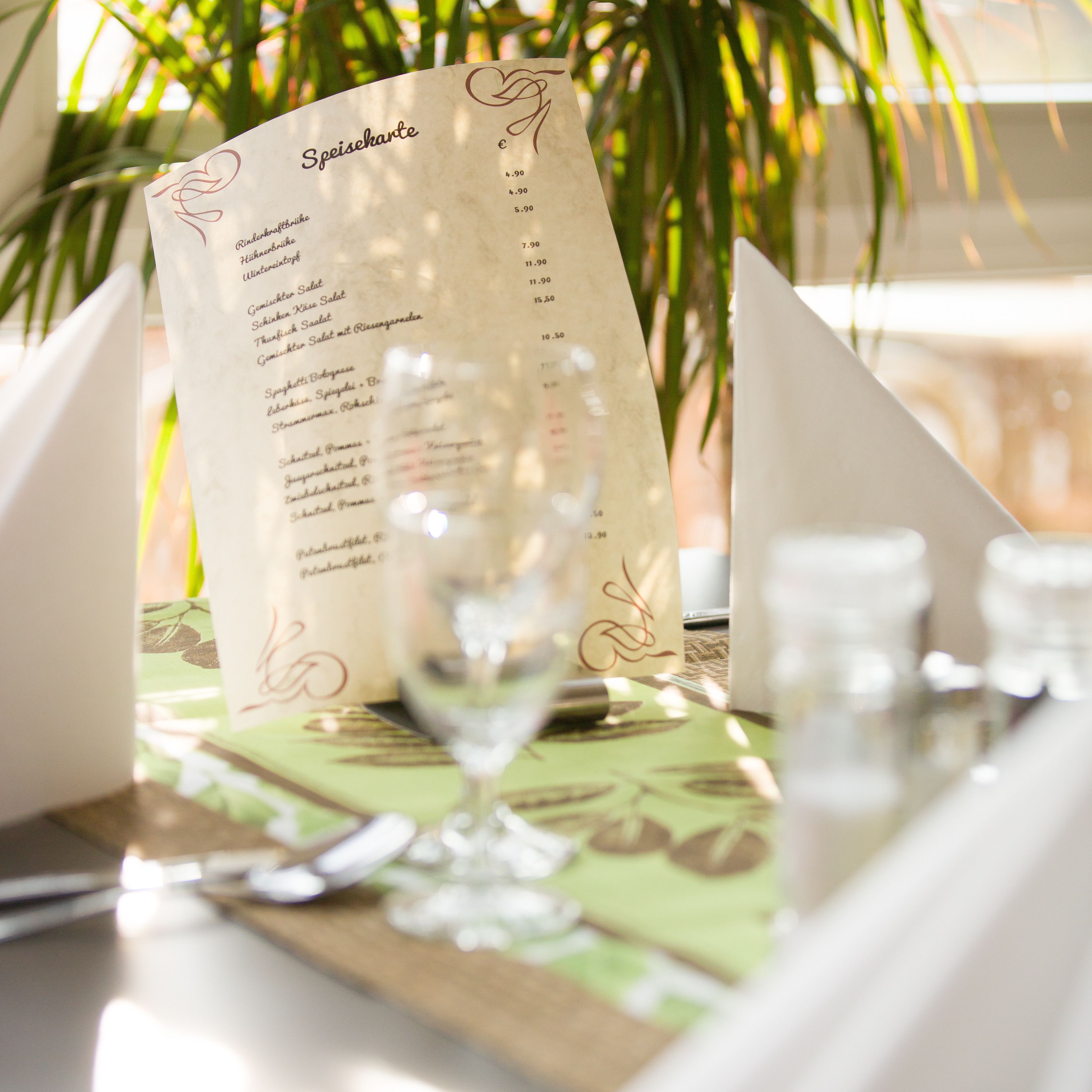 A menu with various dishes and their prices, placed on a table with a green tablecloth.