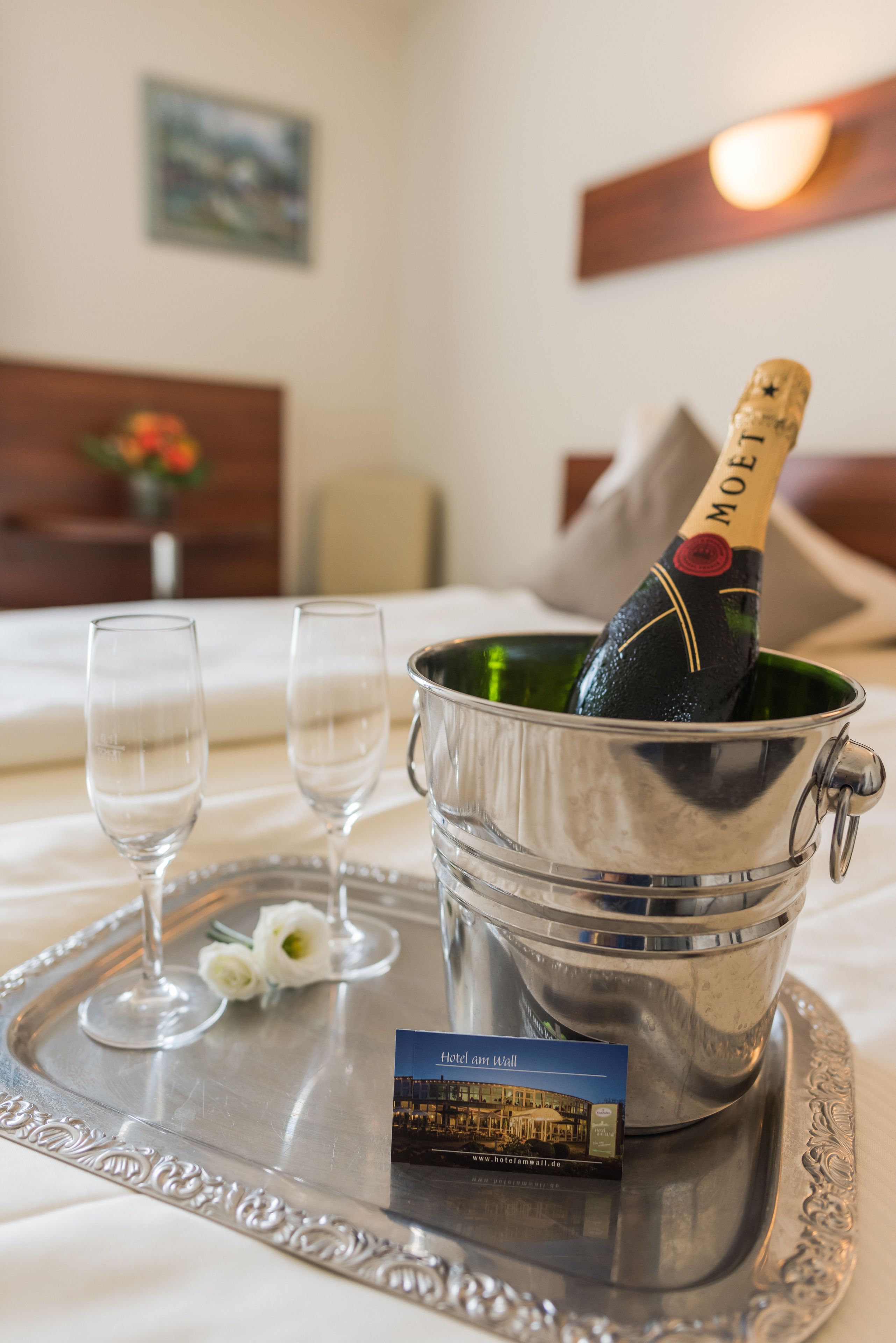 Een bed met een metalen dienblad waarop een champagnefles, twee glazen en een hotelbrochure staan.