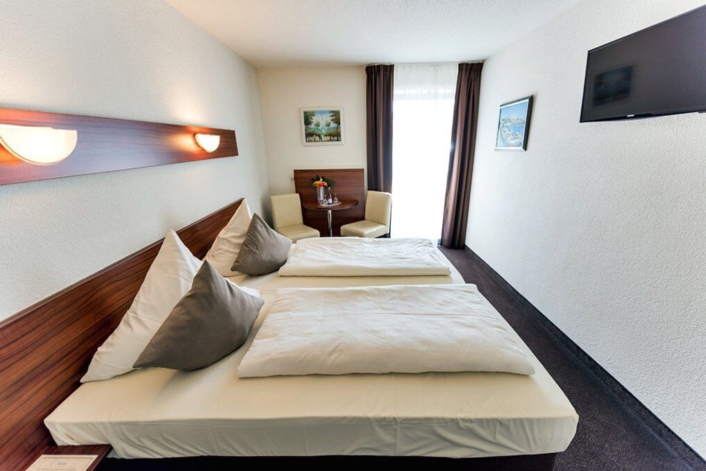 A hotel room with two beds, a desk, a chair, and a TV.