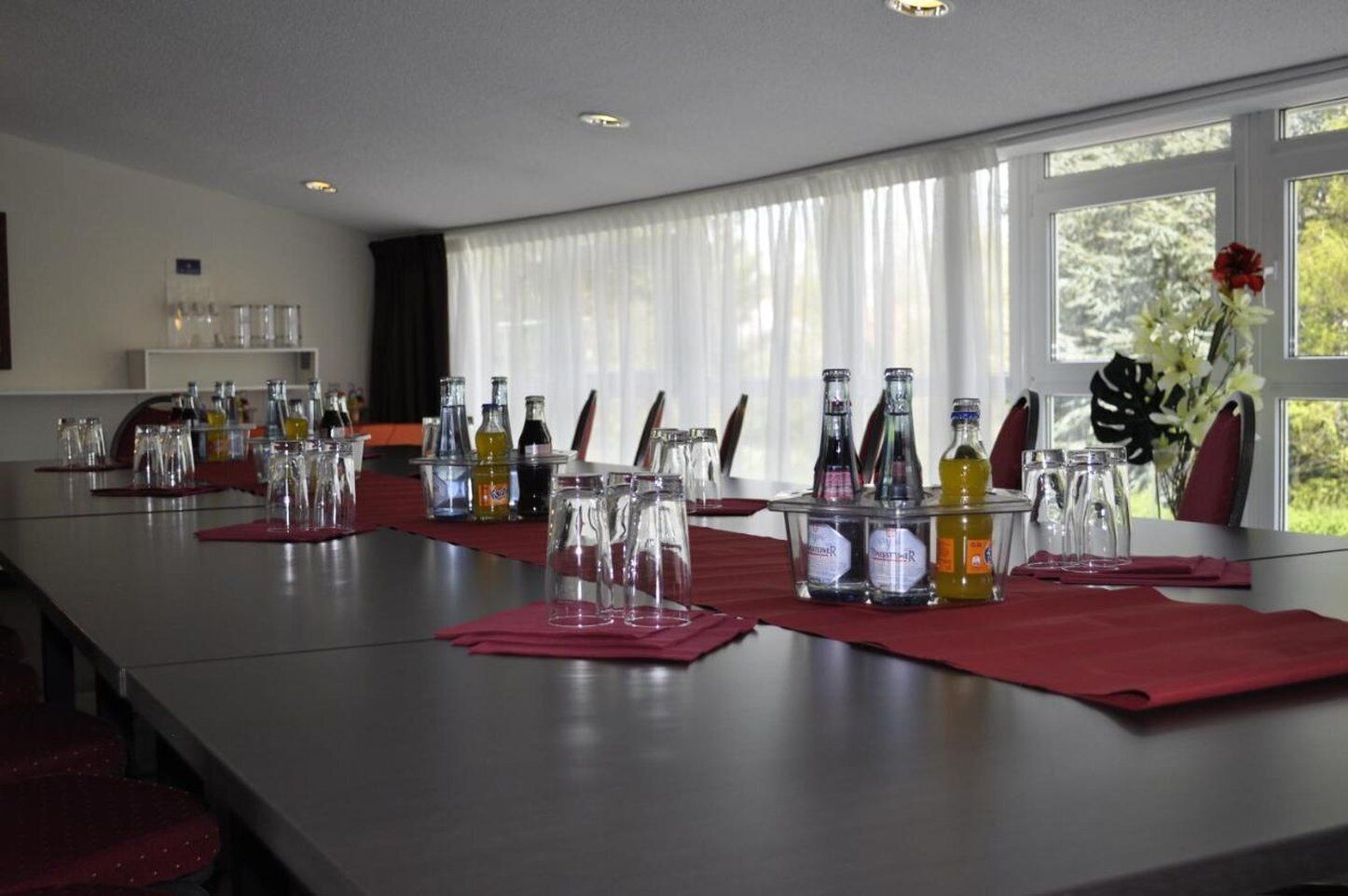 A conference room with a long table set for a meeting, equipped with glassware and bottles, and large windows with curtains.