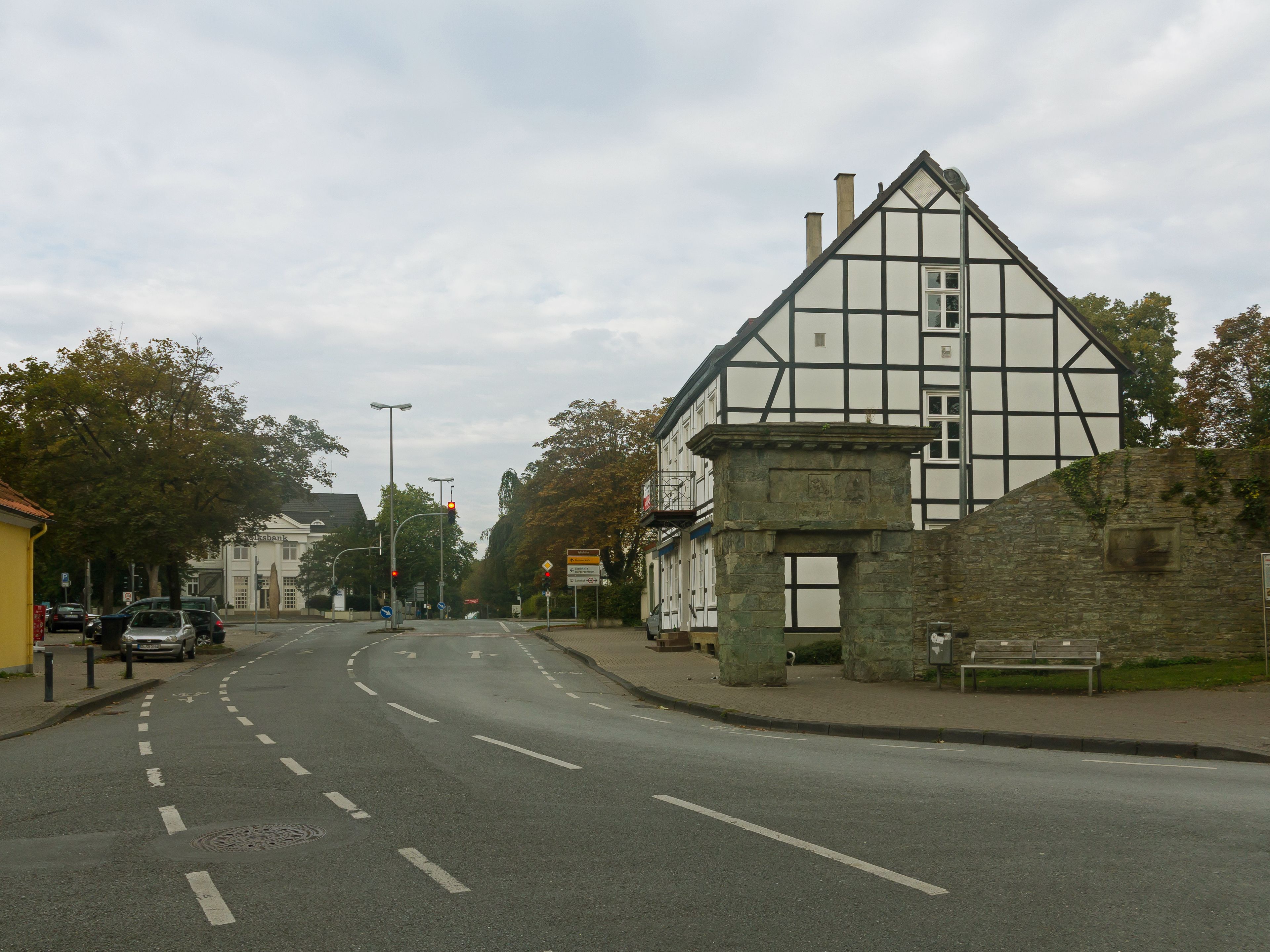 A road with a white building with black trim and a stone wall on the right.