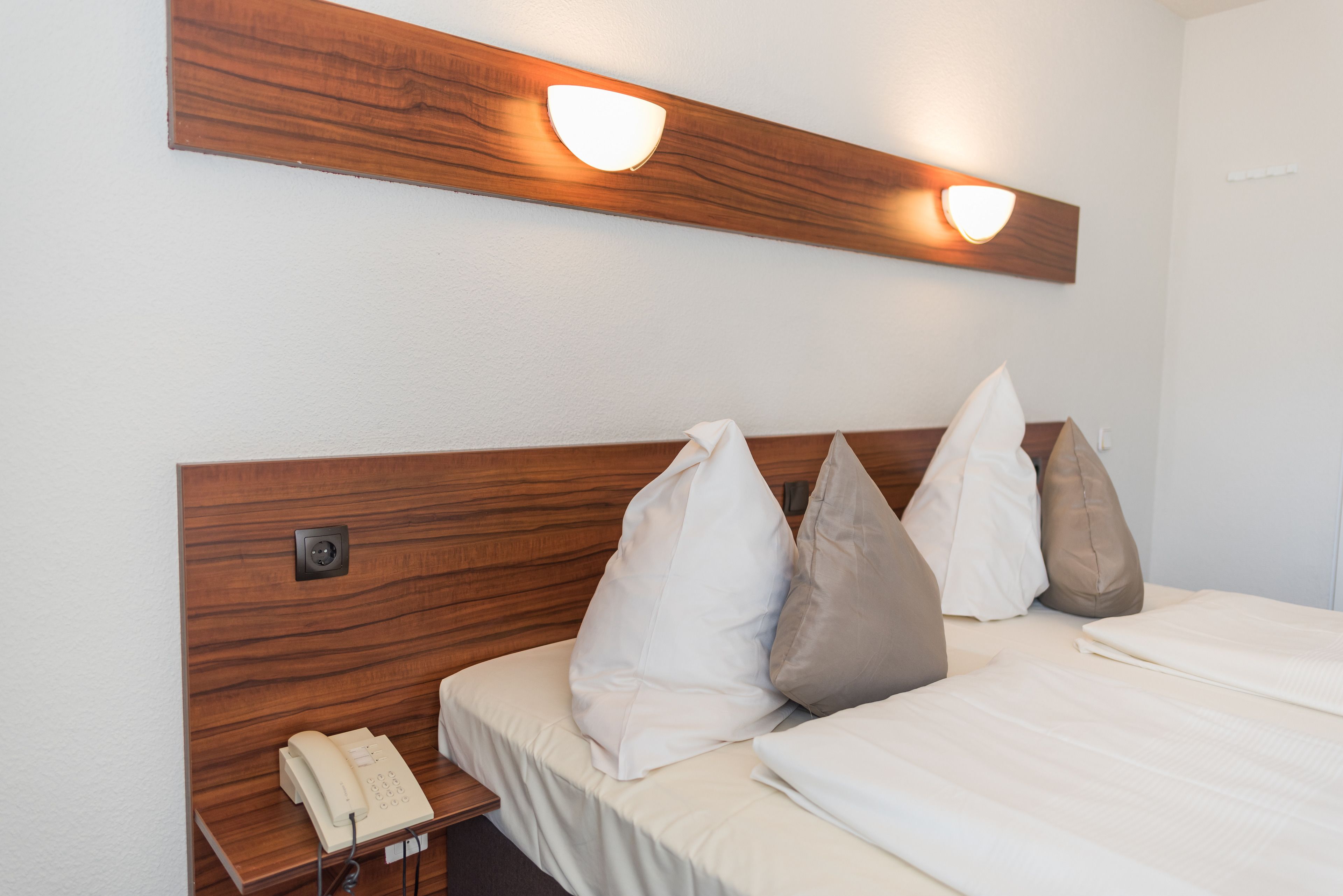 Habitación de hotel con cabecera de madera, teléfono junto a la cama y ropa de cama blanca.