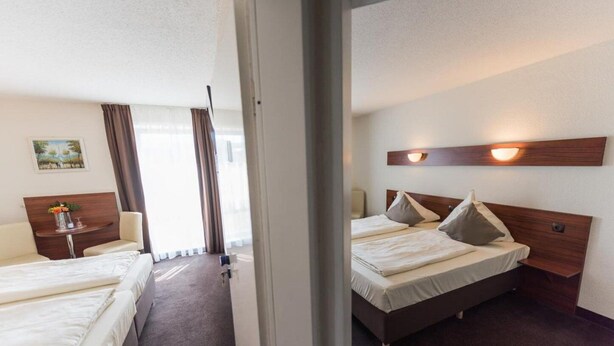 A hotel room with two beds, a desk, a chair, and a window with curtains. - Hotel Am Wall Soest (Soest)