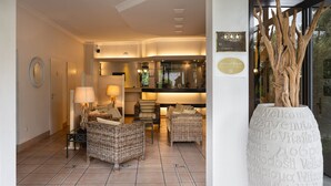 Un vestíbulo de hotel con muebles de mimbre, un mostrador de recepción y un gran jarrón decorativo con texto.