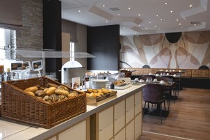 Un buffet de petit-déjeuner comprenant un panier en osier rempli de pain, un plateau en bois garni de viennoiseries et un comptoir avec des assiettes et des tasses.