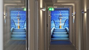 Un pasillo con paredes espejadas que reflejan una vista de una torre y escaleras mecánicas.