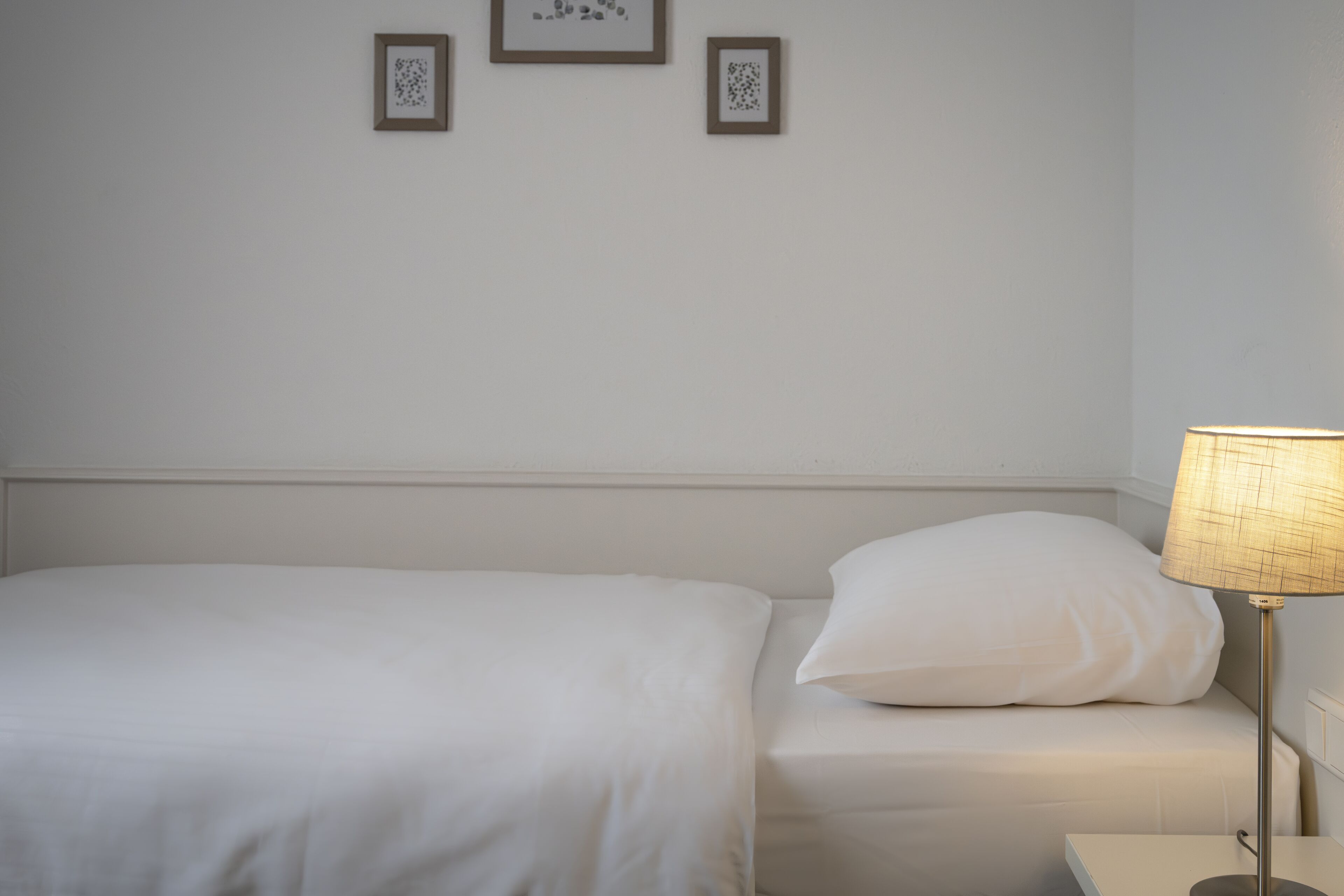 A neatly made bed with white bedding and a single pillow, a bedside lamp, and two framed pictures on the wall.
