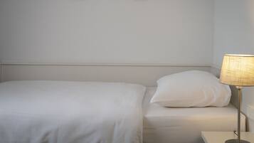 A neatly made bed with white bedding and a single pillow, a bedside lamp, and two framed pictures on the wall.