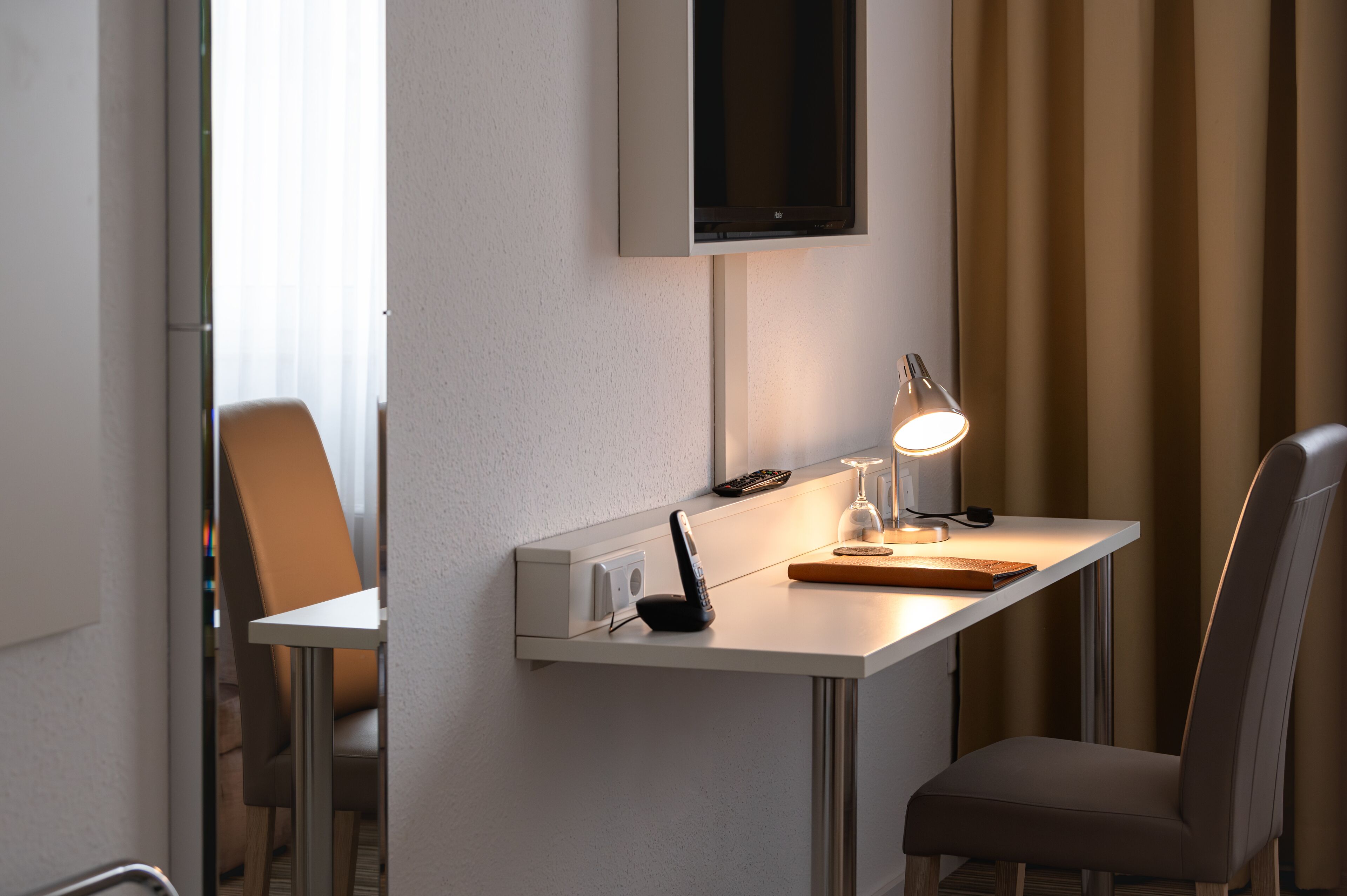Une chambre d’hôtel moderne équipée d’un bureau, d’une chaise et d’un téléviseur fixé au mur.