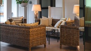 Una habitación con mobiliario de mimbre, incluyendo un sofá y sillones, lámparas y una planta en maceta.