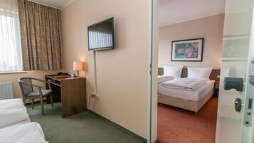 A hotel room with a bed, a desk with a chair, a TV mounted on the wall, and a painting on the wall.