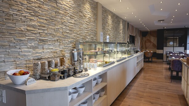 Una barra de desayuno moderna con un fondo de pared de piedra, varios alimentos y una zona de estar con mesas y sillas.