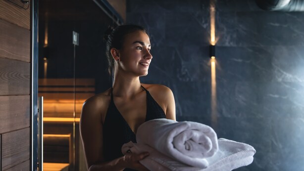 A person holding a rolled towel in a room with wooden walls and a dark, textured wall in the background.
