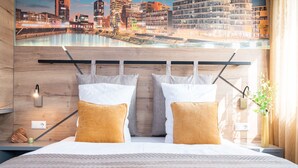 A modern hotel room with a bed, two pillows, a nightstand, a lamp, and a view of a cityscape through a large window.