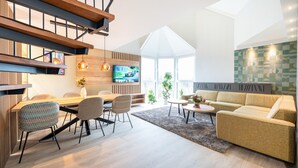 A modern living room with a wooden staircase, a dining area, a sofa, and a TV.