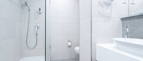 Ein modernes Badezimmer mit einer gläsernen Duschkabine, einem weißen Waschbecken und einem an der Wand befestigten Föhn.