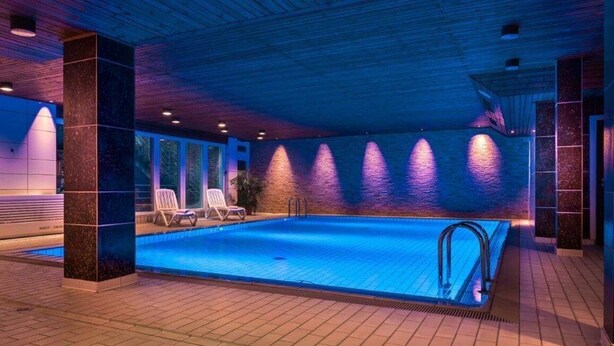 An indoor swimming pool with a tiled floor, a pool ladder, and a few lounge chairs. - Hotel Am Stadtpark (Hilden)