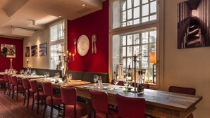 A restaurant with long wooden tables and red chairs, large windows, and artwork on the walls. - Hotel Am Stadtpark (Hilden)