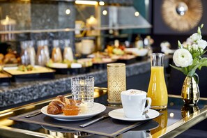 Un bufé de desayuno con cruasanes, jugo de naranja y una taza de café sobre una bandeja.