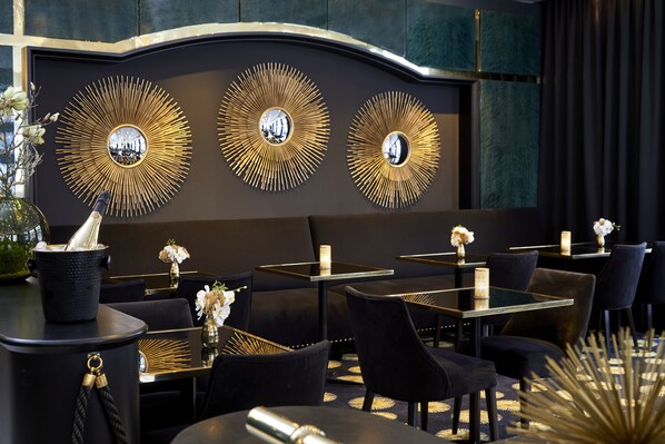 A modern restaurant interior with black and gold decor, including wall-mounted mirrors and tables with black chairs.