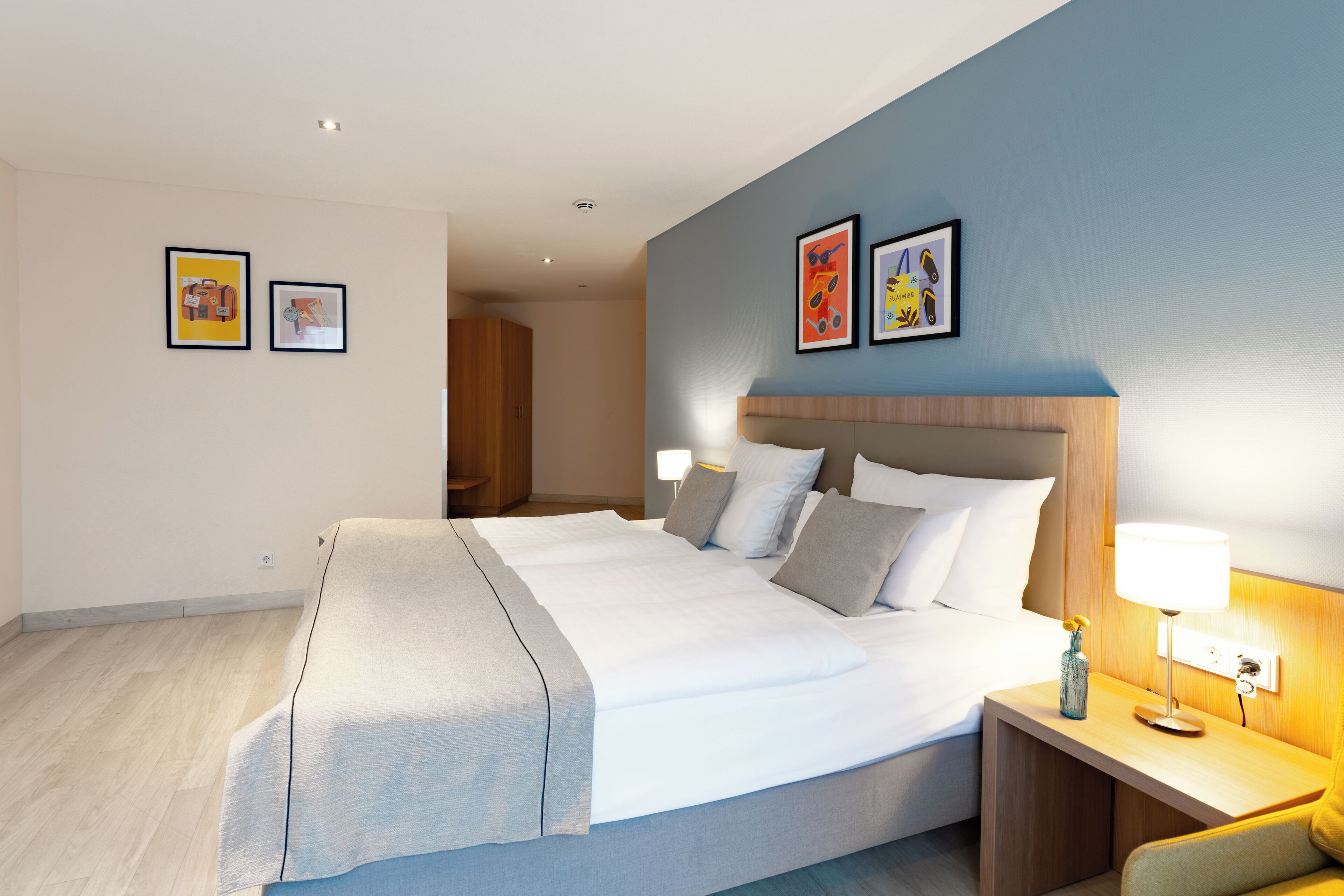 A modern hotel room with a large bed, bedside tables, and artwork on the walls.