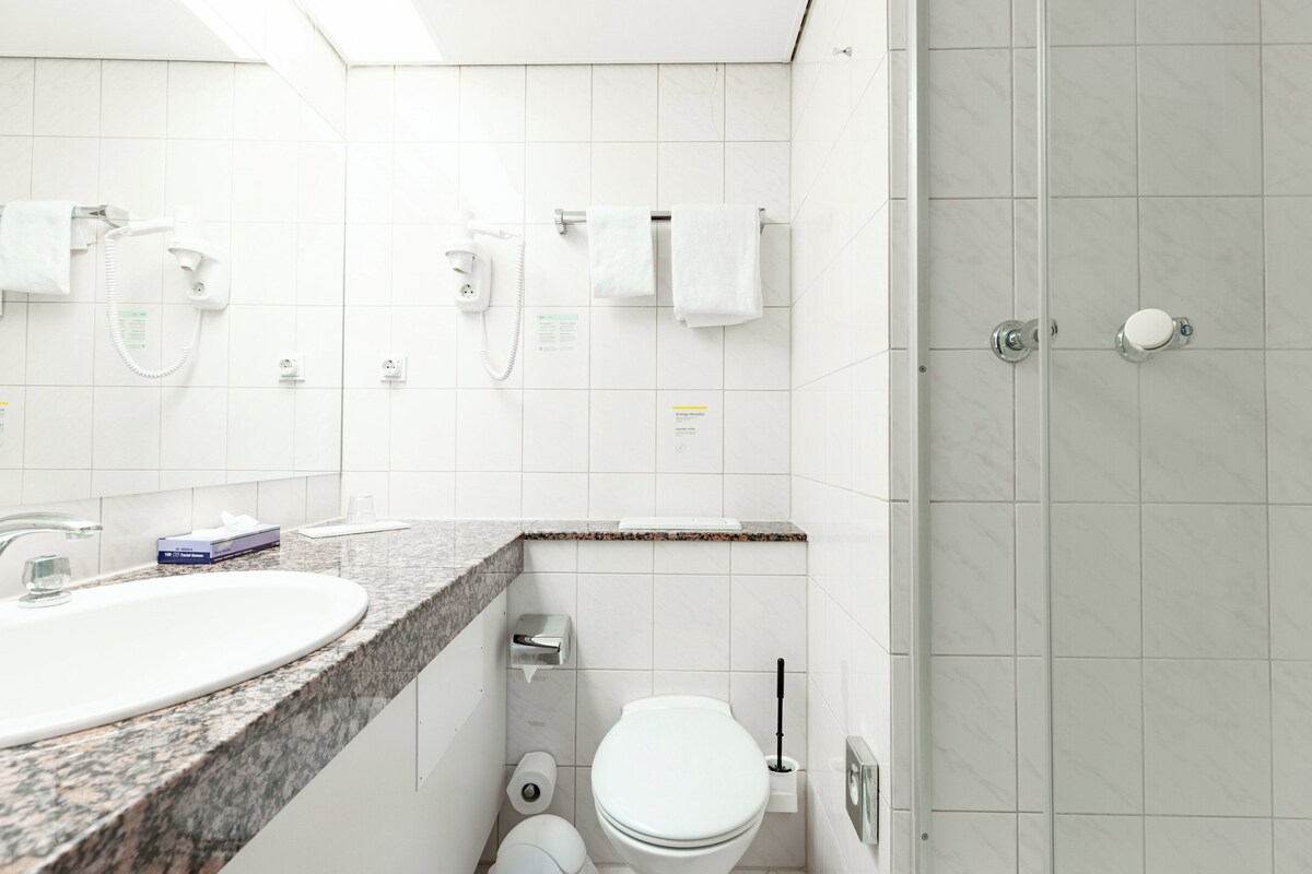 Un bagno moderno con lavandino su piano in granito, un water e una doccia con porta in vetro, e un telefono.