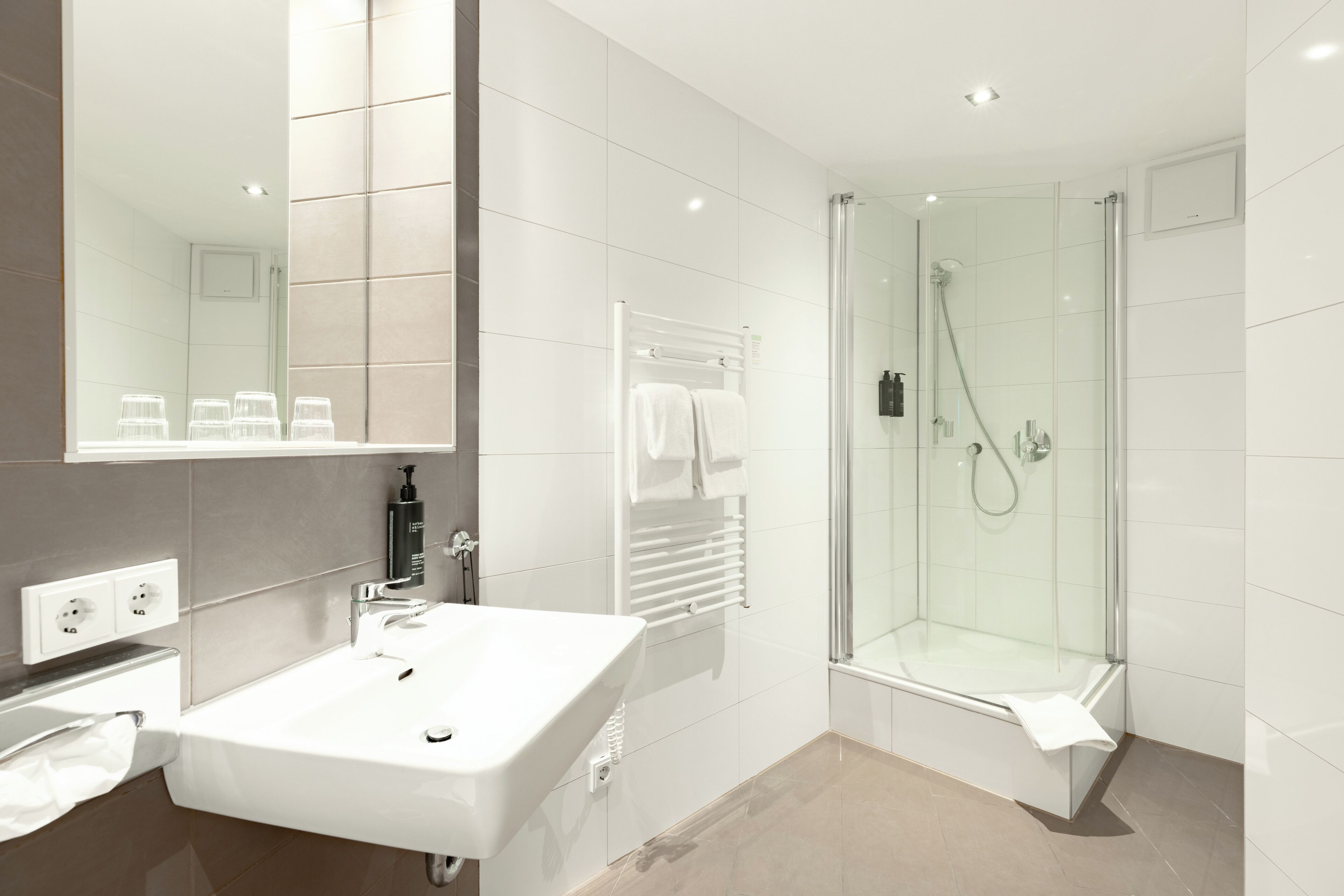 Un baño moderno con un lavabo blanco, cabina de ducha de vidrio y un espejo grande.