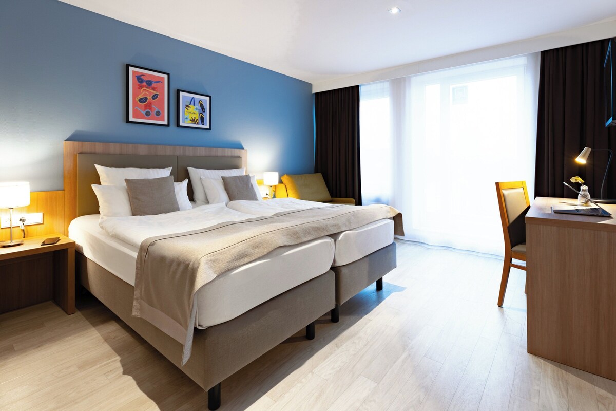 Una camera d'albergo moderna con un letto grande, comodini con lampade, una scrivania e una sedia.