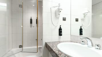Un baño moderno con ducha de vidrio, un lavamanos blanco con encimera de granito y dos secadores de pelo blancos fijos en la pared.