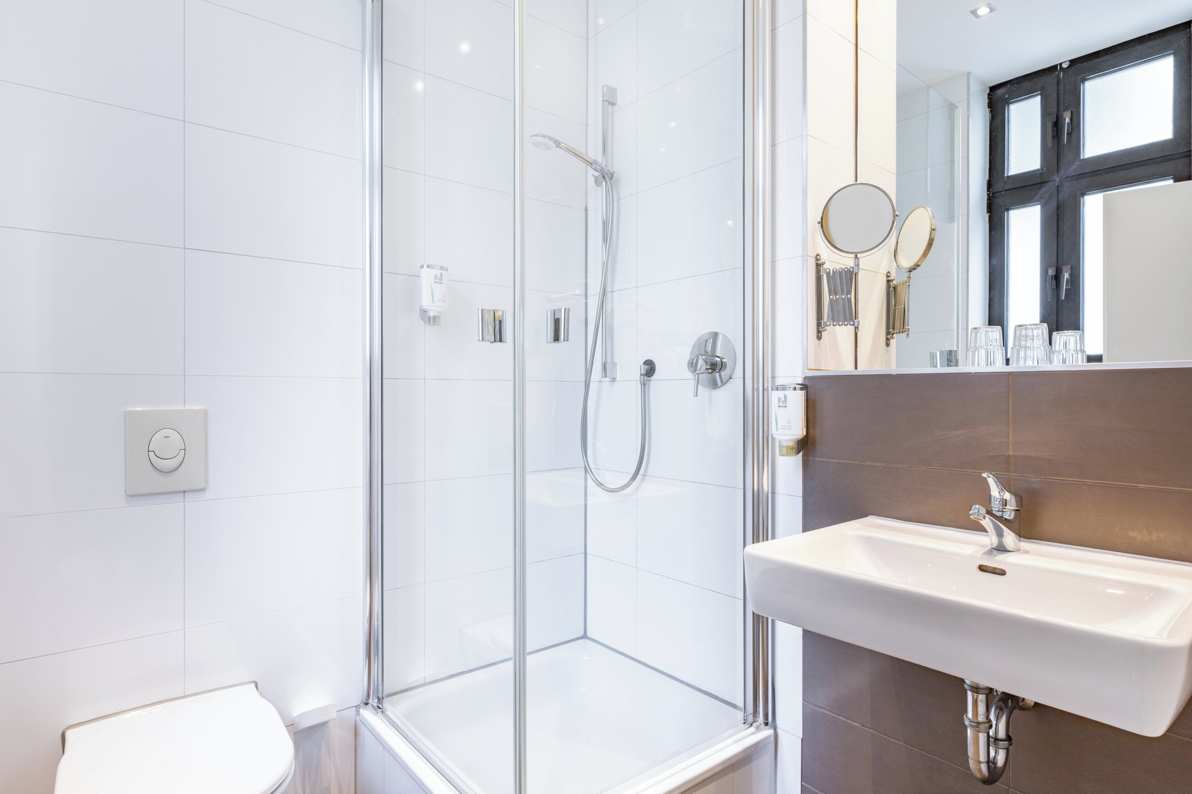 A modern bathroom with a glass-enclosed shower, a white sink, and a mirror with a round frame.