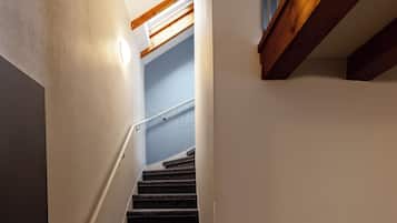 Una scala con struttura in travi di legno, ringhiera e un lampadario a parete.