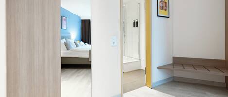A modern hotel room with a bed, a shower area, and a bench.
