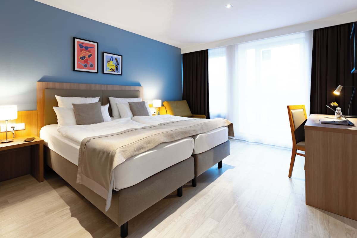 A modern hotel room with a large bed, bedside tables with lamps, a desk, and a chair.