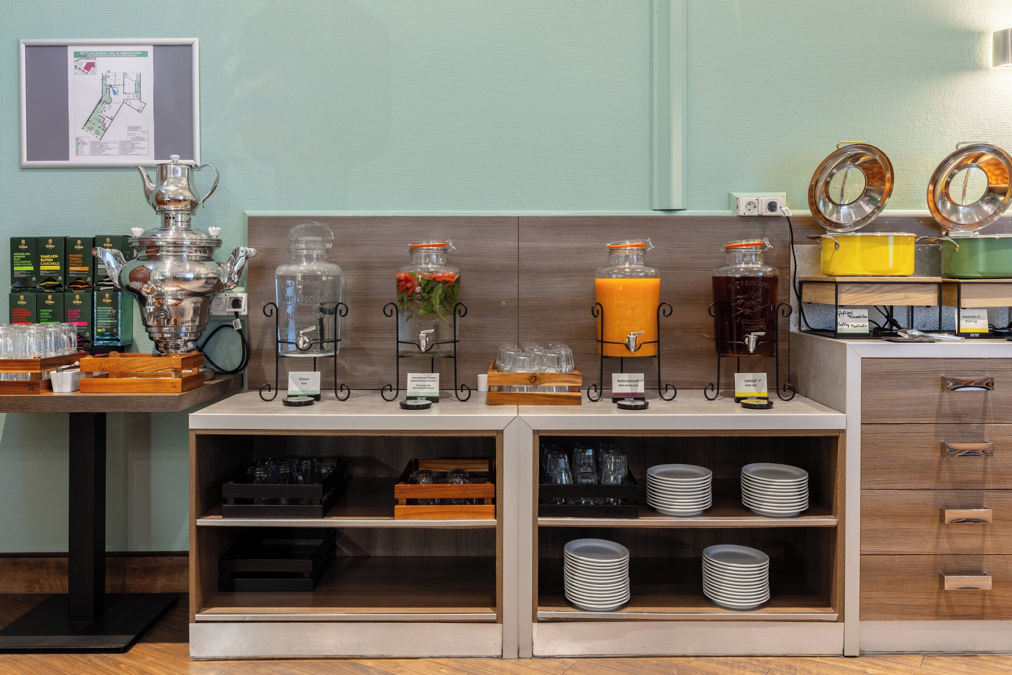 A breakfast buffet setup with various food and drink dispensers, a coffee machine, and a map on the wall.