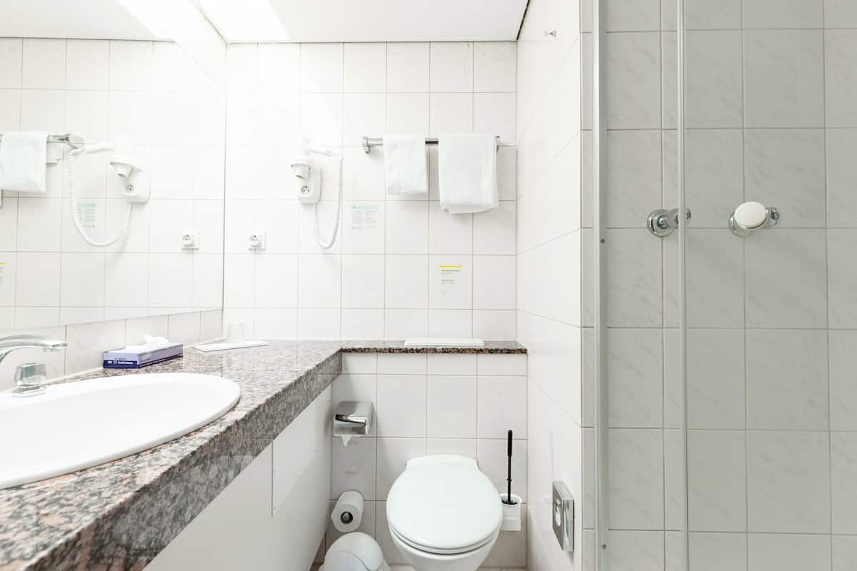 A modern bathroom with a granite countertop sink, a toilet, a shower with a glass door, and a telephone.