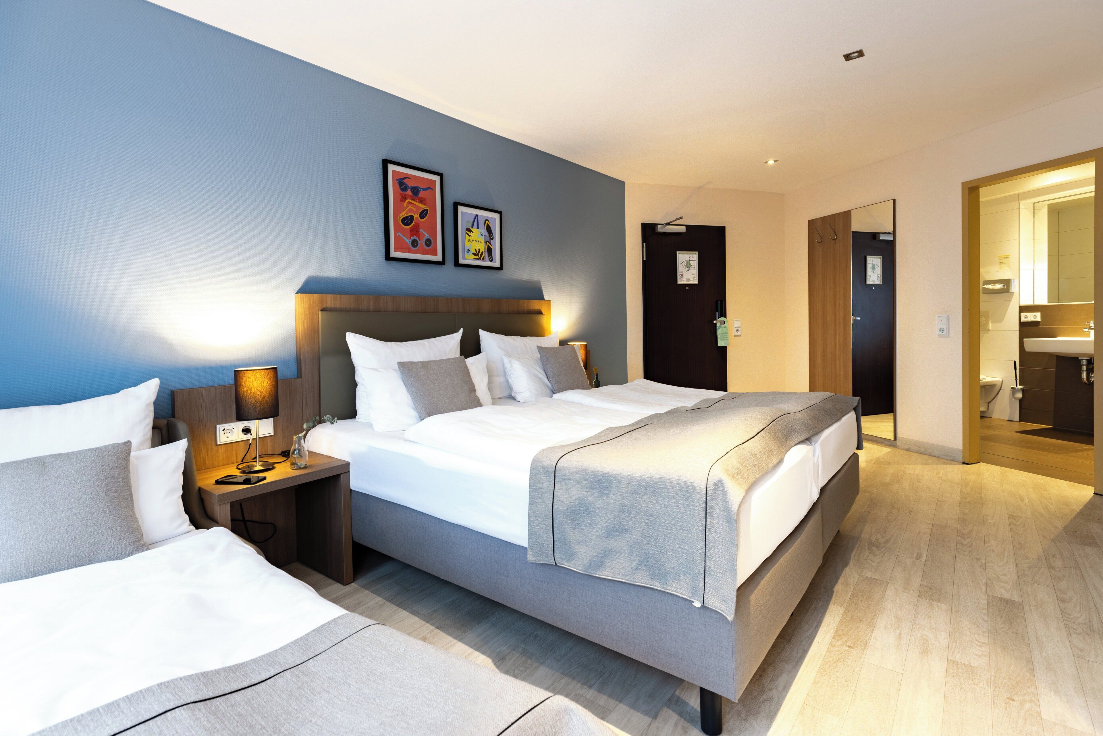Una habitación de hotel moderna con una cama grande, mesitas de noche y un baño visible a través de una puerta abierta.