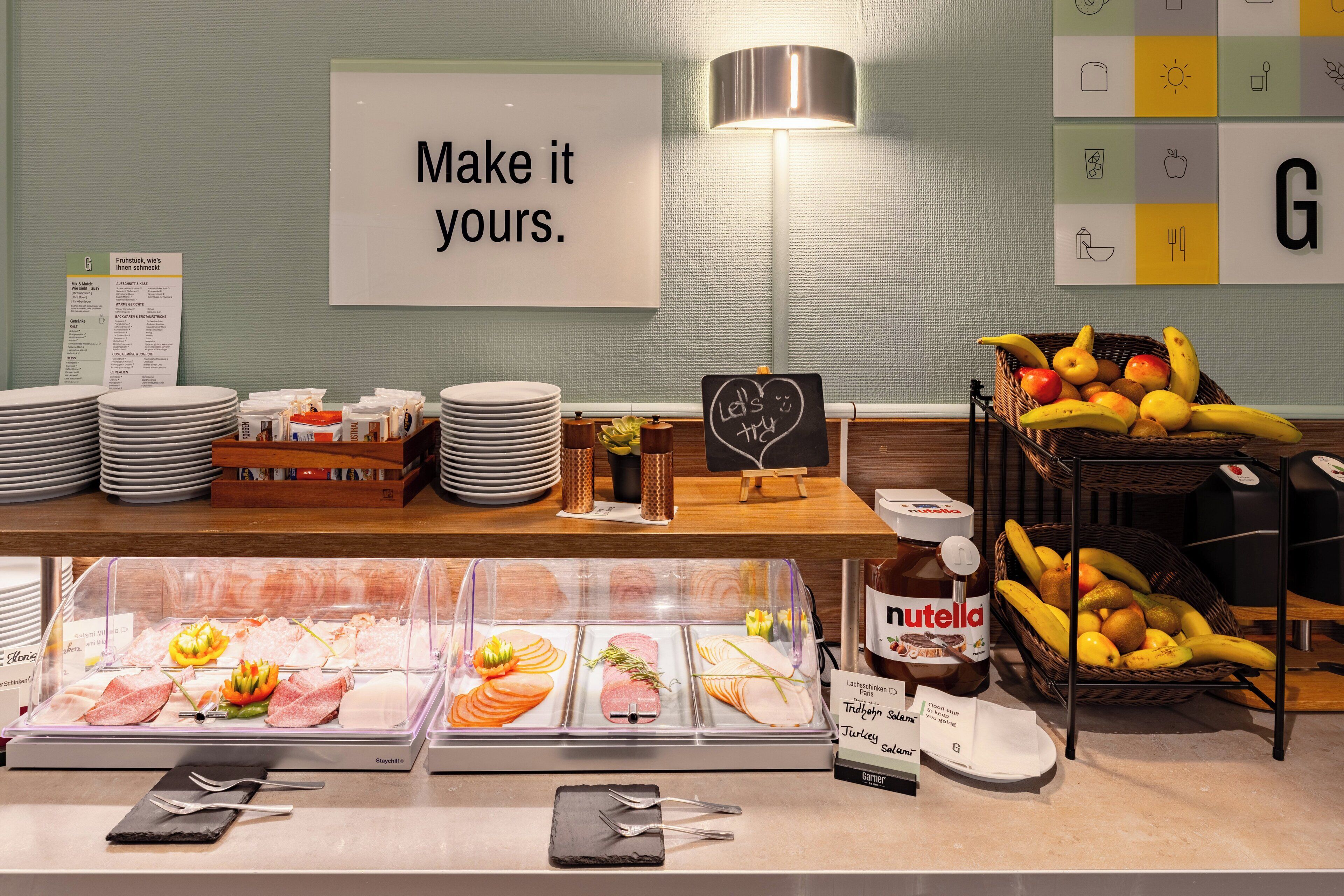 A buffet area with various food items, a sign that says "Make it yours.", and a basket of fruits.